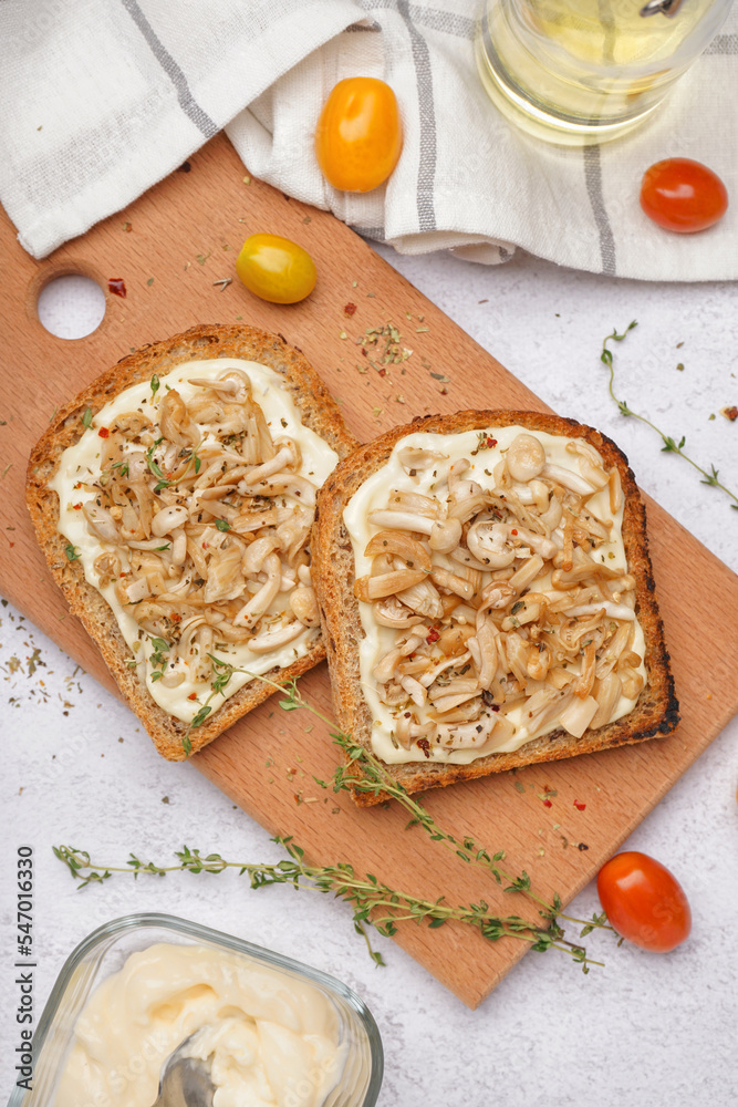 Wooden board of tasty toasts with cream cheese, mushrooms and tomatoes on light background