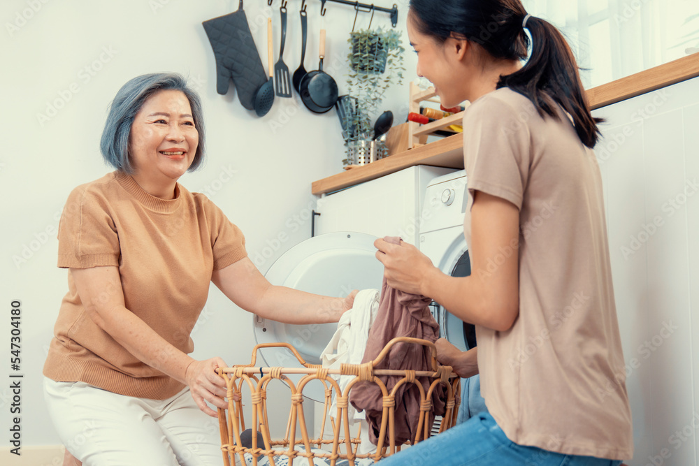 Daughter and mother working together to complete their household chores near the washing machine in 