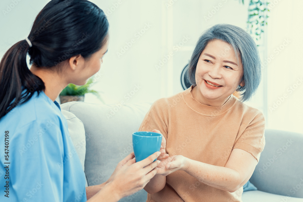 女性护理人员在家里为满足的老年患者端上一杯咖啡，对每个人微笑