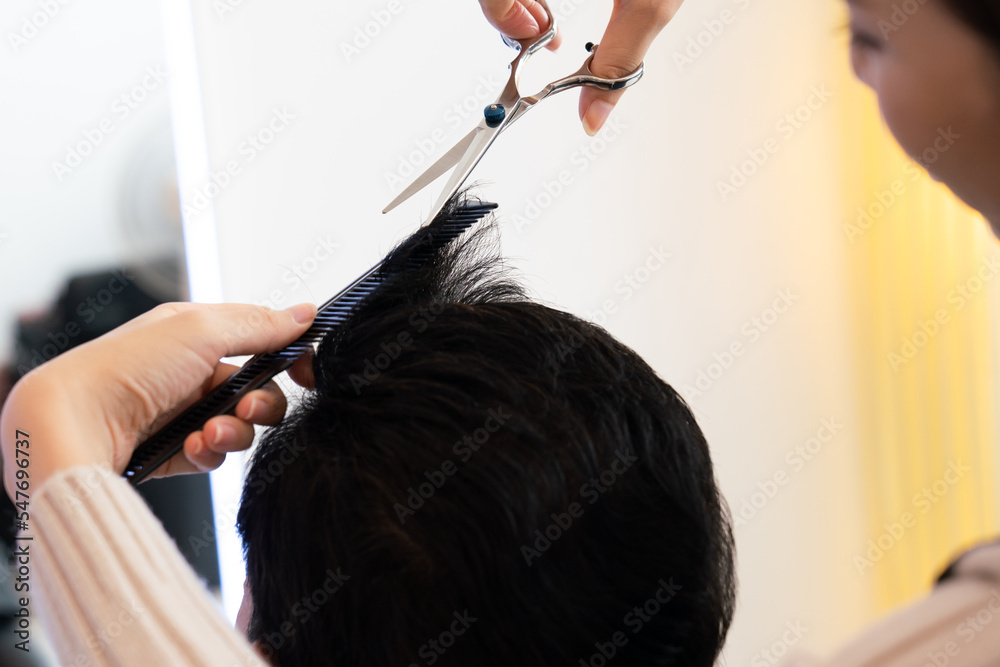 Closeup asian female barber making haircut for male customer with male hairstyle in qualified barber