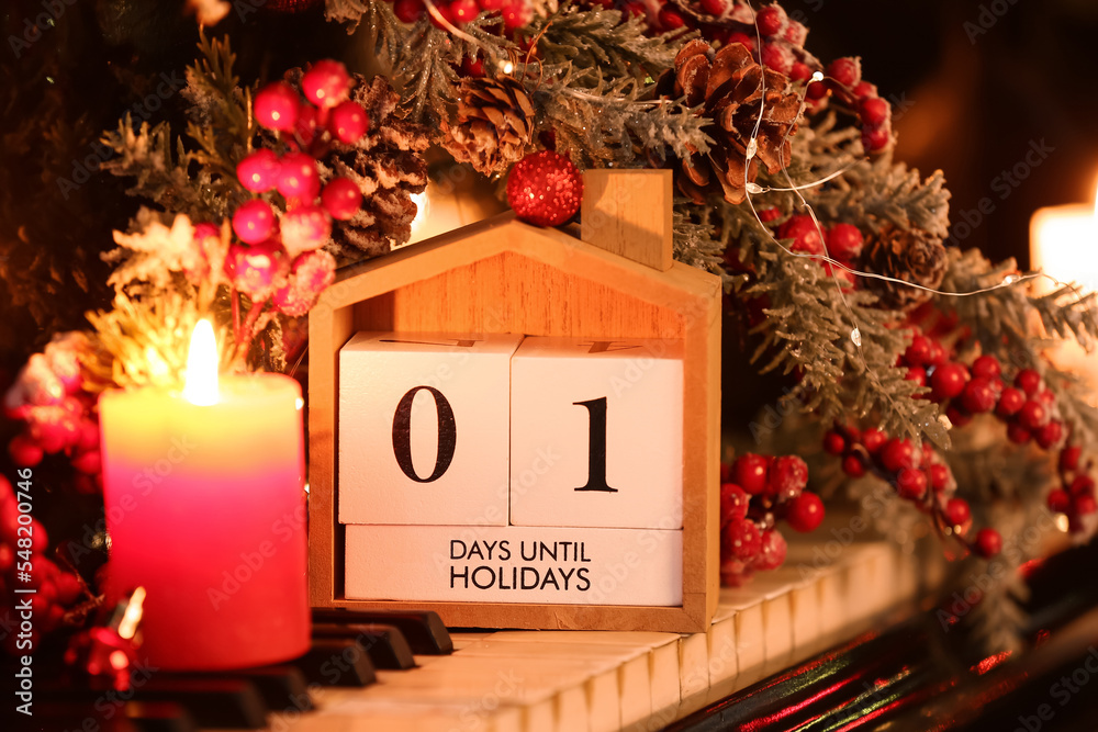 Calendar with text 1 DAY UNTIL HOLIDAYS, candle and Christmas decor on piano keys, closeup