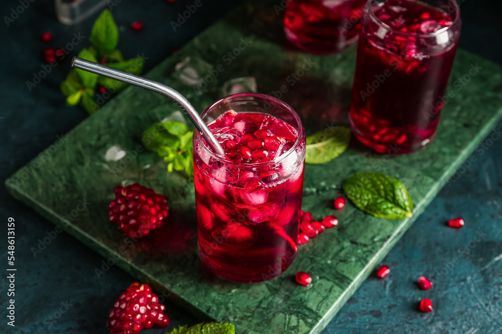 Board with glasses of cold pomegranate juice on dark color background