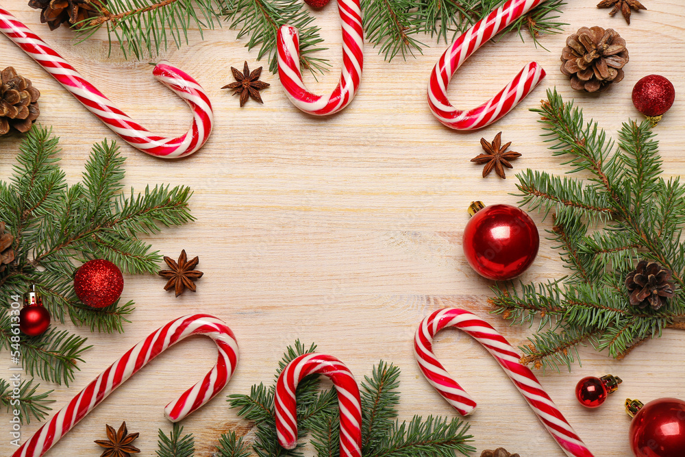 Frame made of sweet candy canes, Christmas balls and fir branches on wooden background