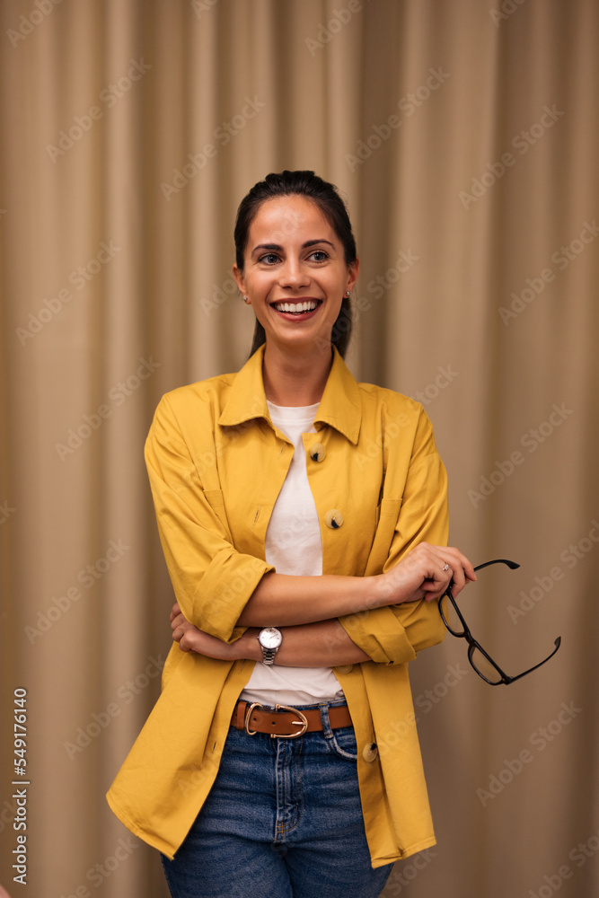 Portrait of a casually dressed woman, looking on the side, smiling, holding glasses.