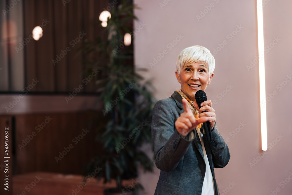 Portrait of a mature woman giving the lecture and a speech, using a microphone.