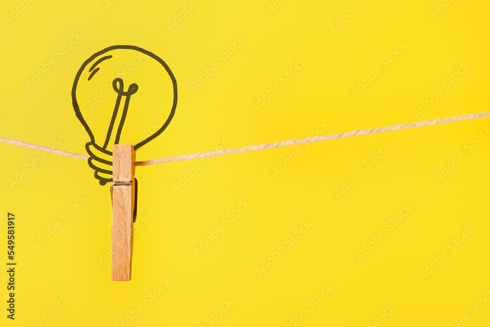 Wooden clothespin with paper light bulb hanging on rope against color background