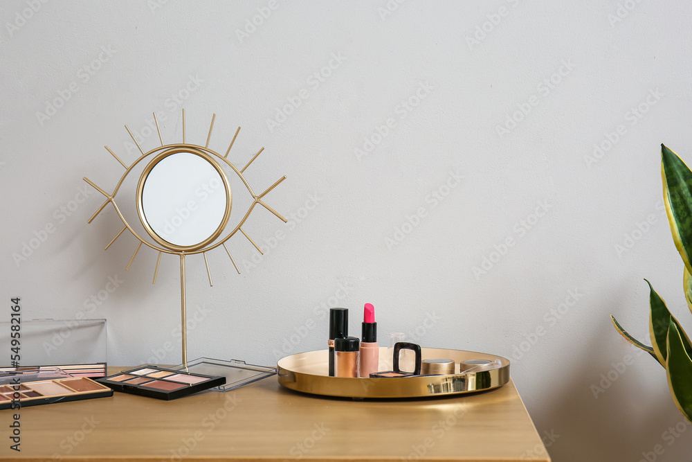 Tray with decorative cosmetics and mirror on wooden table near light wall