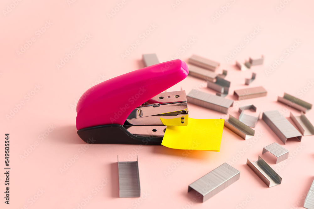 Office stapler with sticky notes and staples on color background