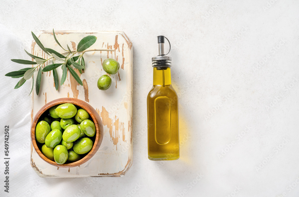 Olives, olive oil in bottle and branch of olive on white wooden board. Mockup for package. Copy spac