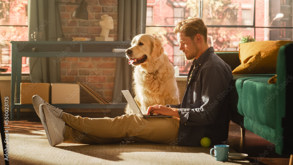 Portrait of a Handsome Young Adult Male Sitting on a Floor and Using Laptop Computer in Sunny Loft L