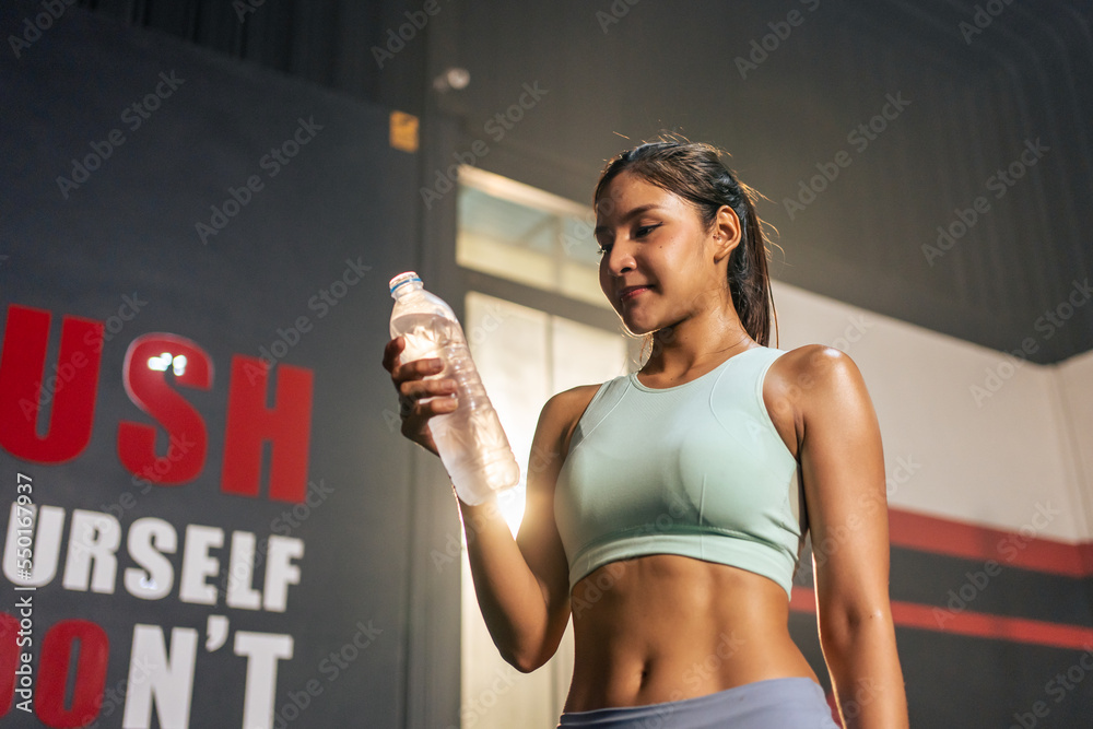 Asian young sportswoman drink a bottle of water after workout in gym. 