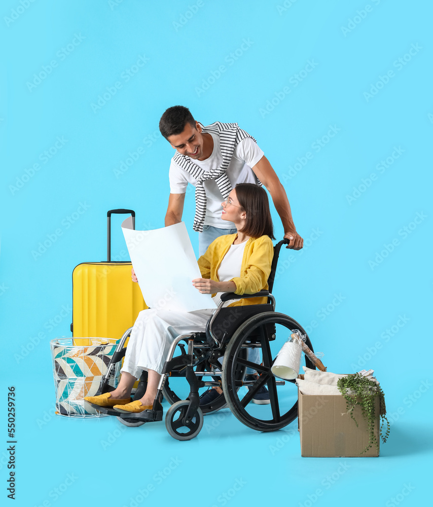 Young man with his wife in wheelchair, moving boxes and house plan on blue background