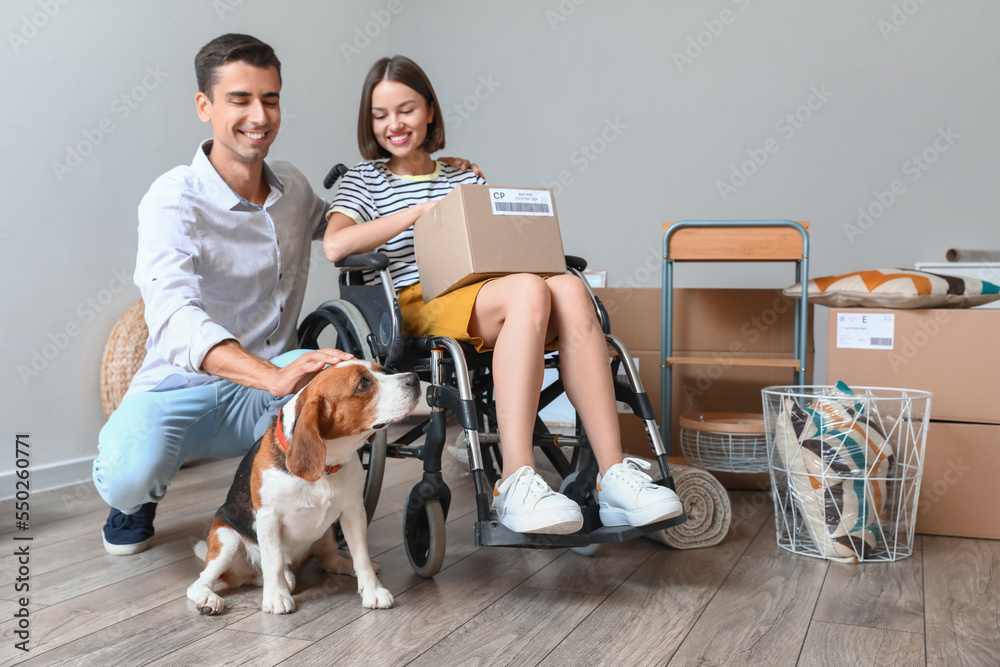 Young man with his wife in wheelchair and dog in their new flat on moving day