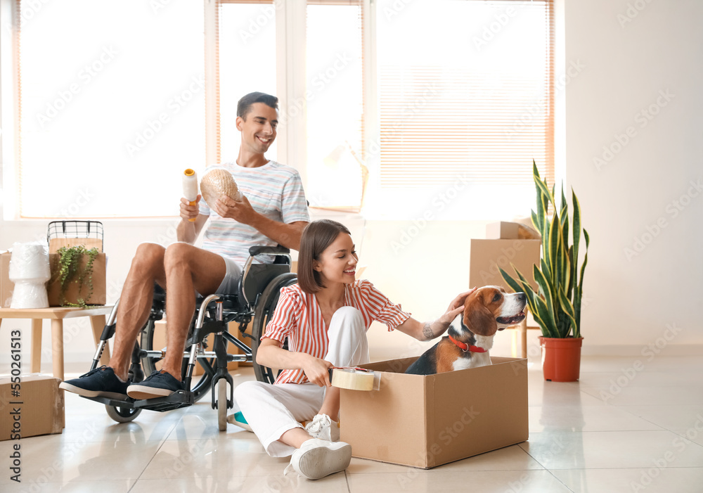 Young woman with her husband in wheelchair and dog packing things in room on moving day