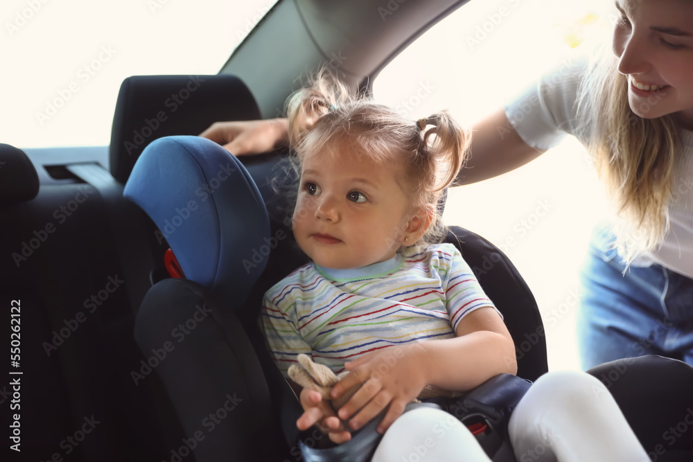 Mother and her little daughter with toy buckled in car safety seat