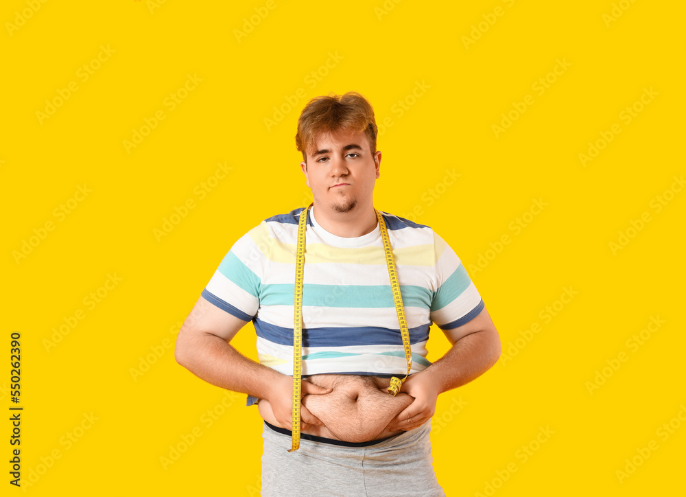 Upset young overweight man with measuring tape on yellow background