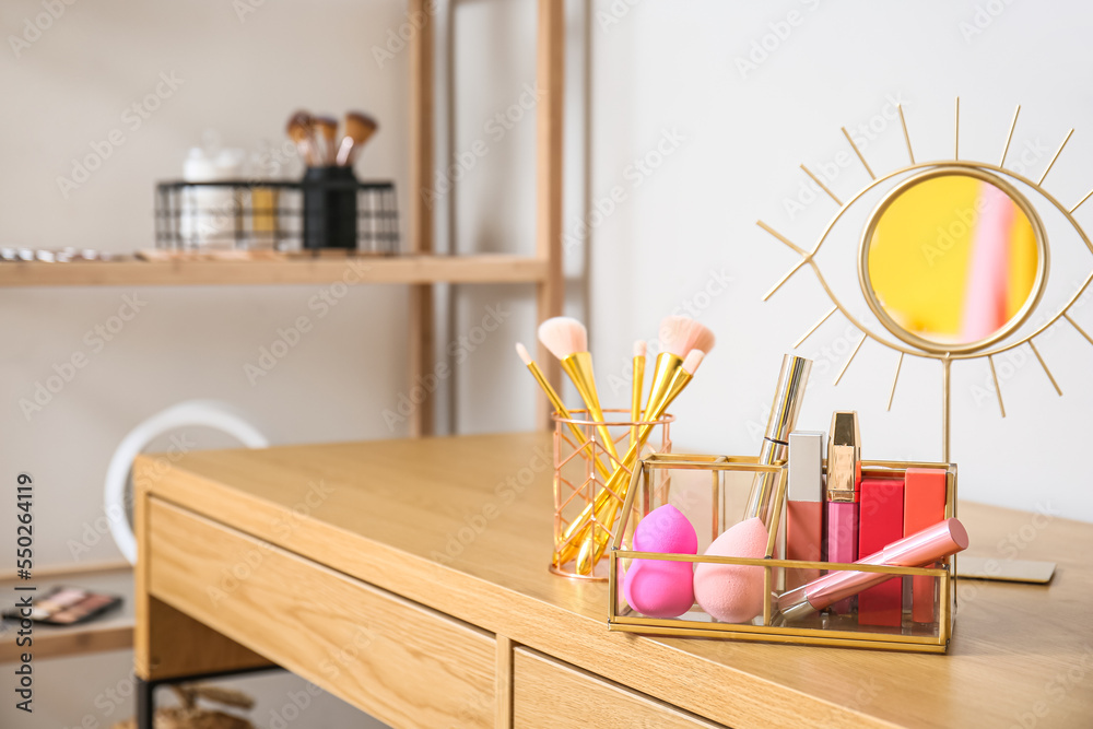 Holders with makeup brushes, sponges and decorative cosmetics on wooden table near light wall