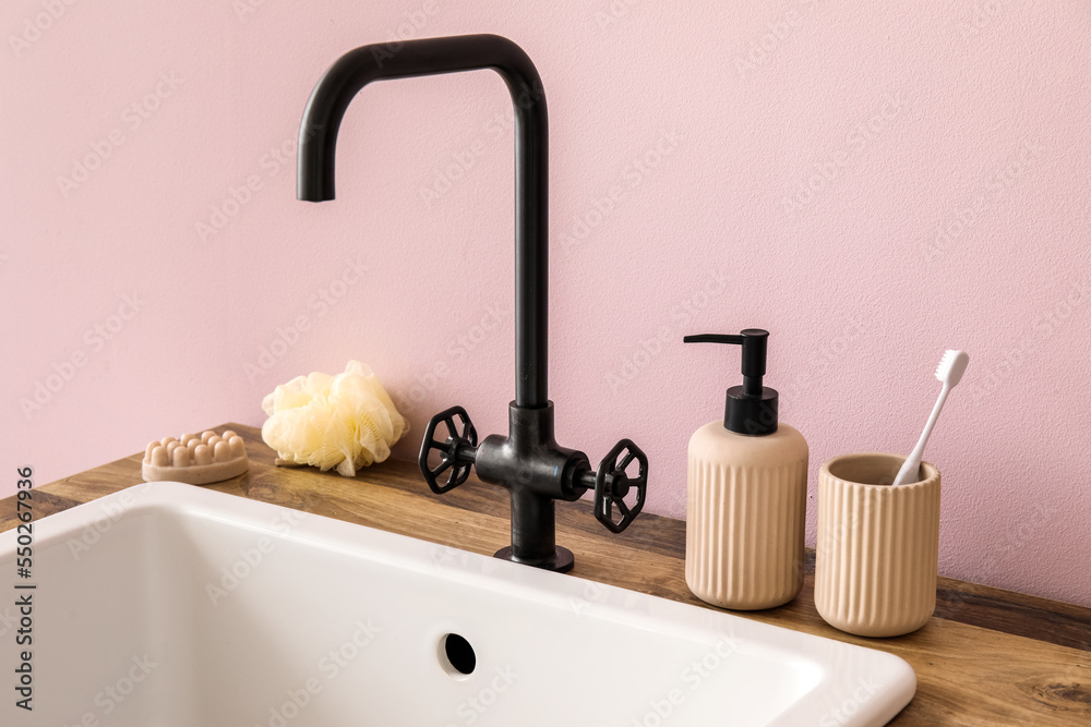 Sink with bath accessories on table near pink wall