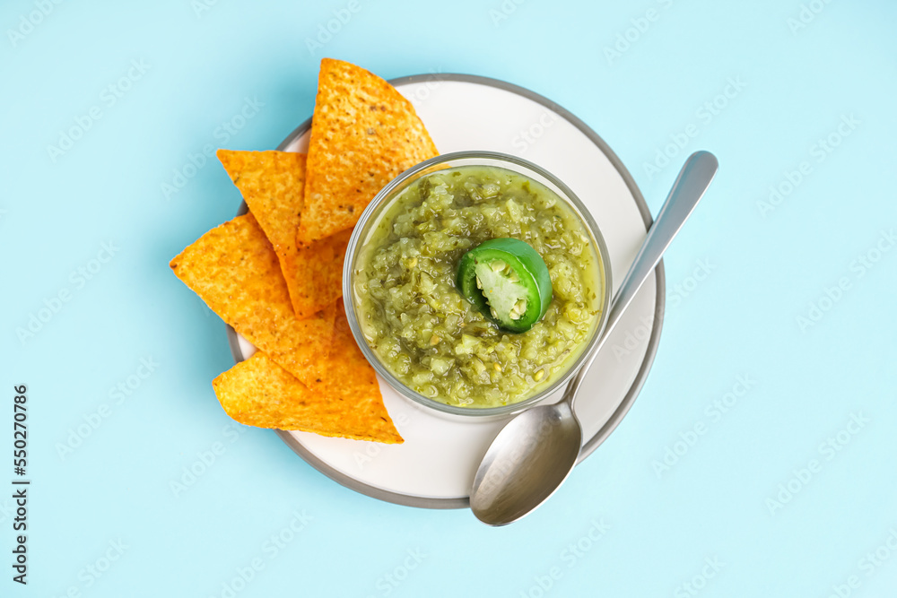 Plate with bowl of tasty green salsa sauce and nachos on color background