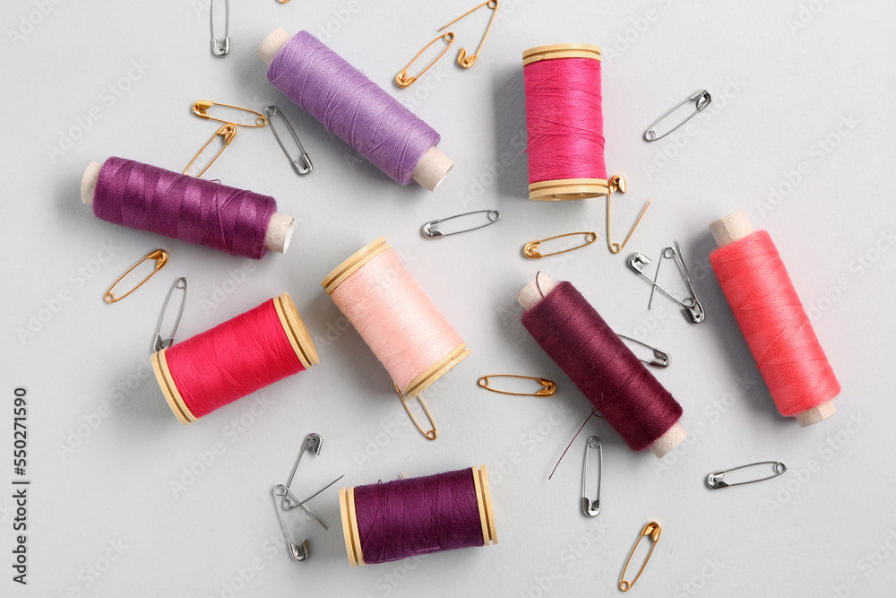 Set of colorful thread spools and safety pins on light background