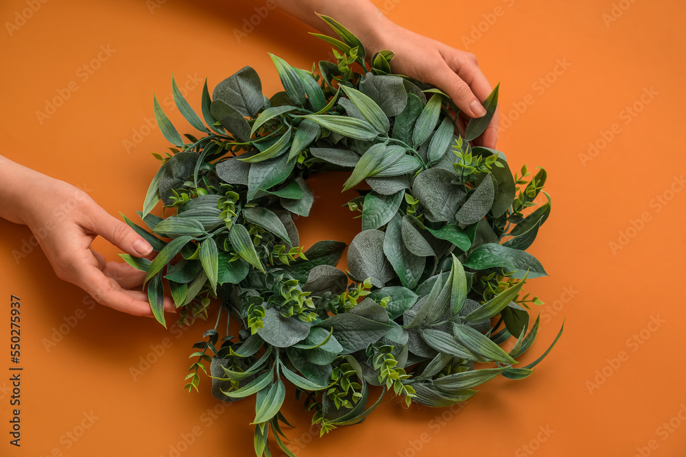 Female hands with stylish Christmas wreath on color background, closeup