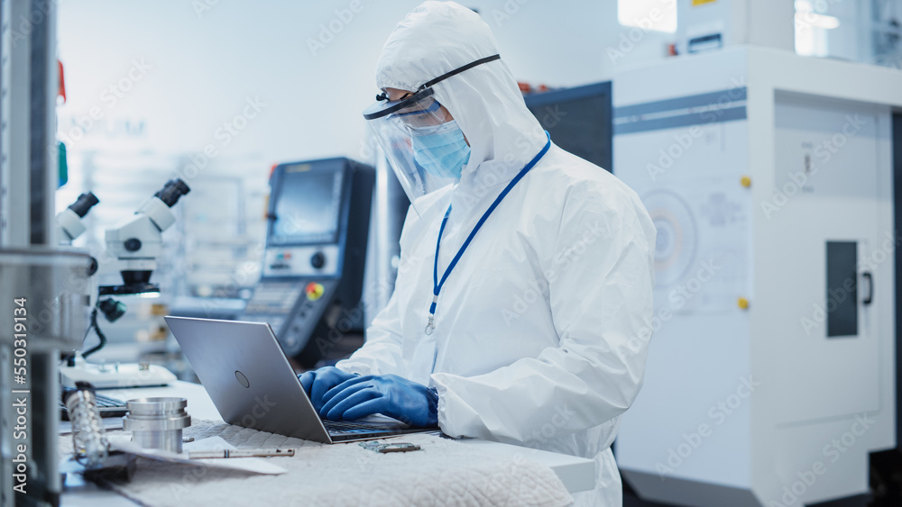 Electronic Manufacturing Factory: Engineer in Sterile Coverall Working on Laptop Computer, Examining