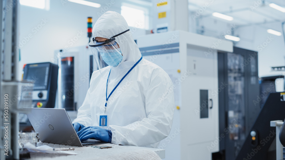 Modern Technology Concept: Engineer in Coverall Working on Laptop Computer, Examining a Circuit Boar