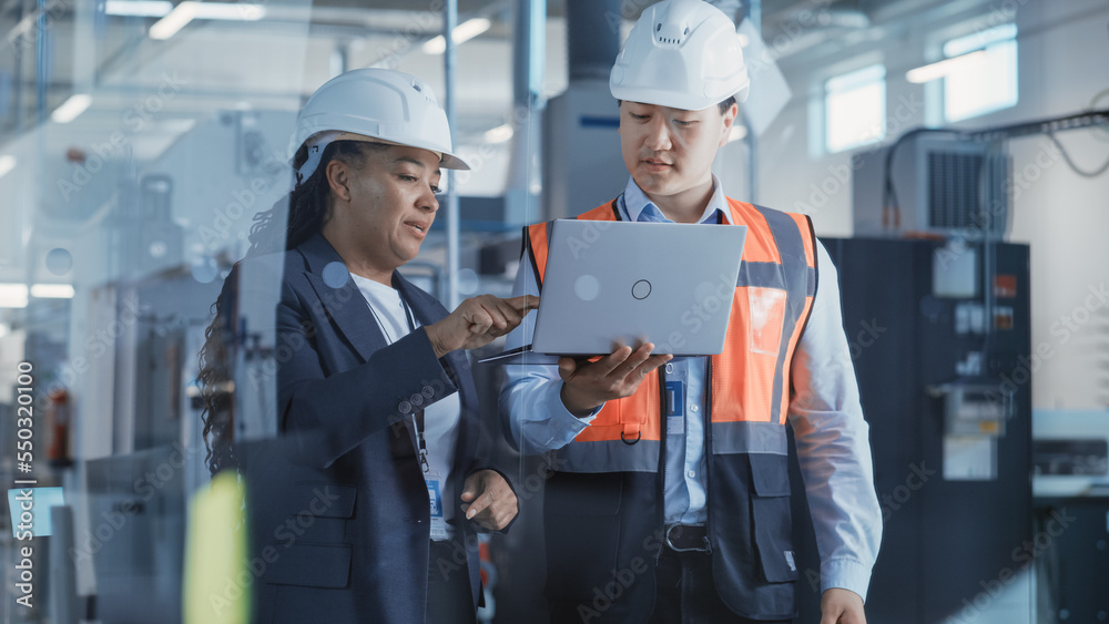 Two Professional Heavy Industry Engineers Wearing Safety Uniform and Hard Hats Discussing Factory Wo