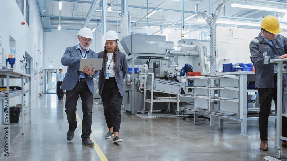 Two Professional Heavy Industry Employees Wearing Hard Hats at Factory. Walking and Discussing Indus