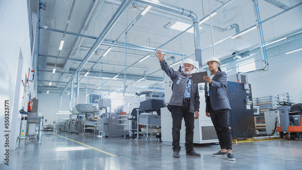 Portrait of Two Heavy Industry Employees in Hard Hats at Factory. Checking and Discussing Industrial