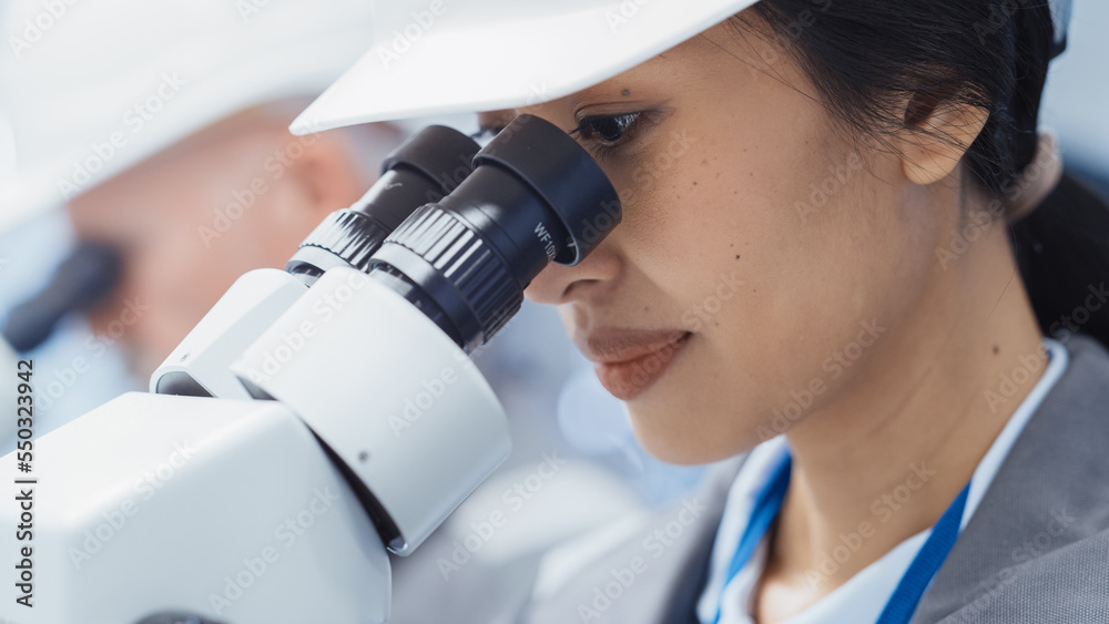 Close Up of a Beautiful Young Asian Industrial Scientist Wearing a White Hard Hat, Working at a Desk