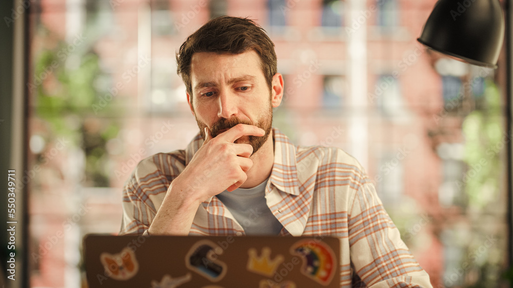 Portrait of a Handsome Man Working on Laptop Computer while Sitting in Stylish Cozy Loft Living Room