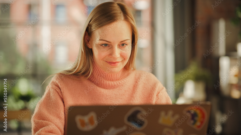 Beautiful Female Working on Laptop Computer while Sitting at a Table in Stylish Cozy Loft Living Roo