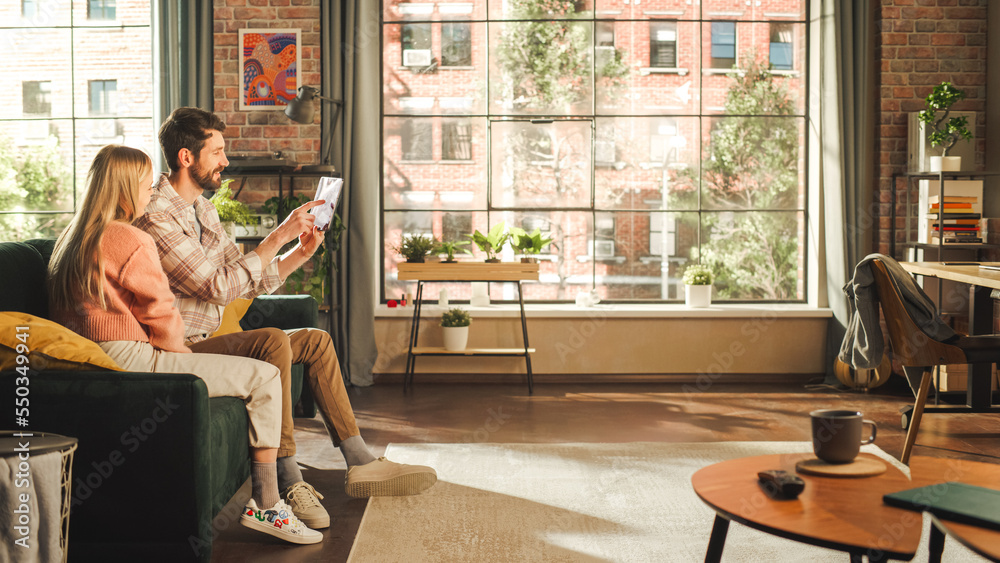 Man and Woman Using Tablet While Sitting on a Couch in a Stylish Apartment. A Young Couple Going Thr