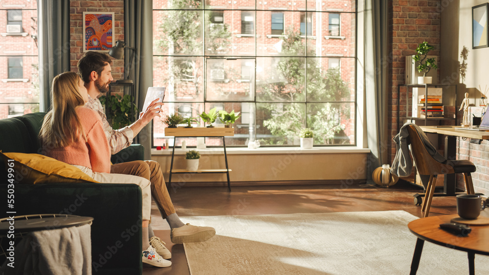 Man and Woman Using Tablet While Sitting on a Couch in a Stylish Apartment. A Young Couple Calling F