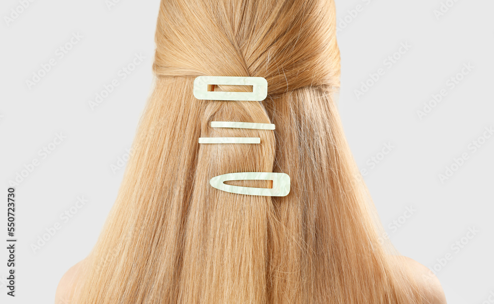 Blonde woman with long hair and stylish hairpins on light background, closeup