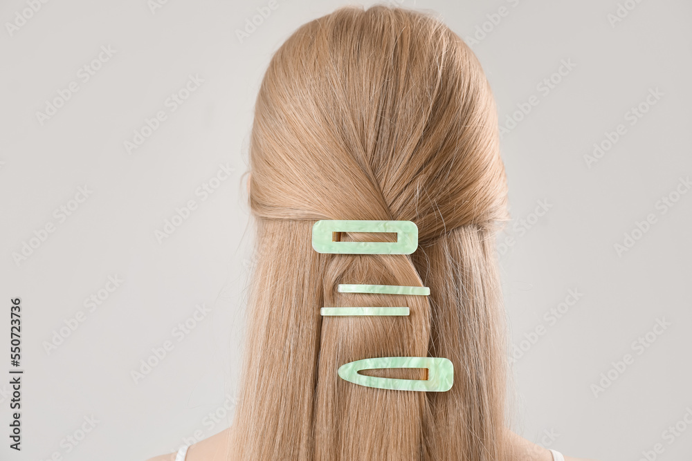 Blonde woman with long hair and stylish hairpins on light background, closeup