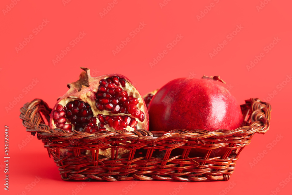 Wicker basket with fresh pomegranates on red background