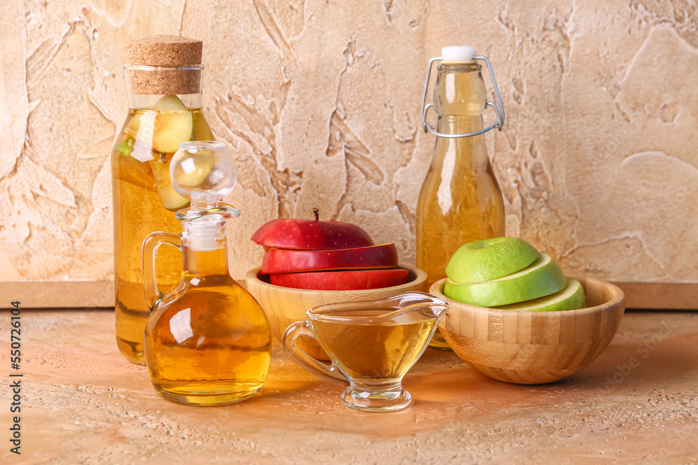 Bottles of apple cider vinegar and fruits on color table