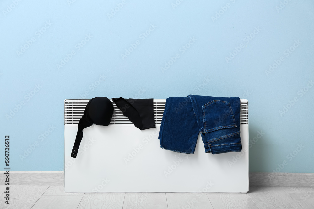 Female underwear and jeans drying on electric radiator near light wall