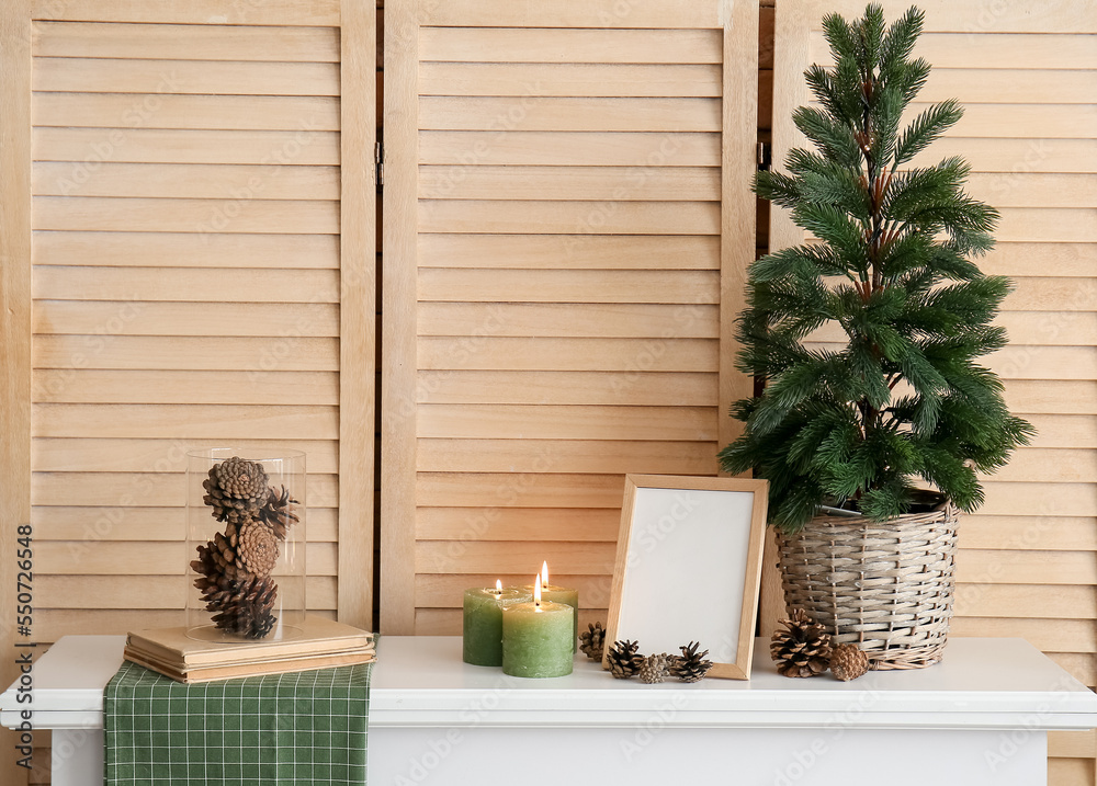 Christmas tree, frame, candles and fir cones on mantelpiece near folding screen