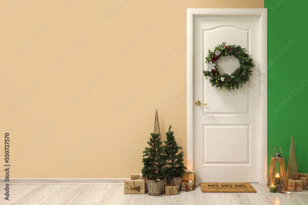 White door with Christmas wreath, fir trees and presents in hall