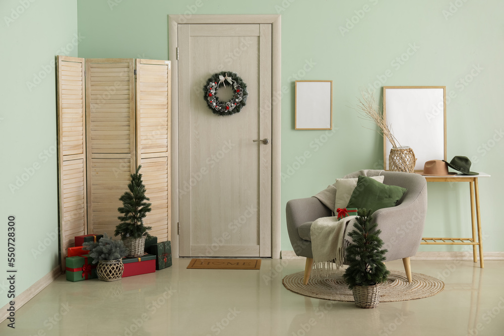 Interior of hall with wooden door, Christmas wreath, trees and armchair