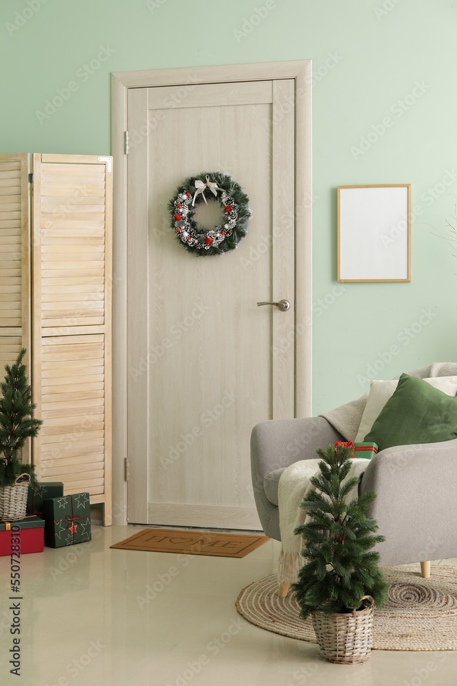 Interior of hall with wooden door, Christmas wreath, trees and armchair