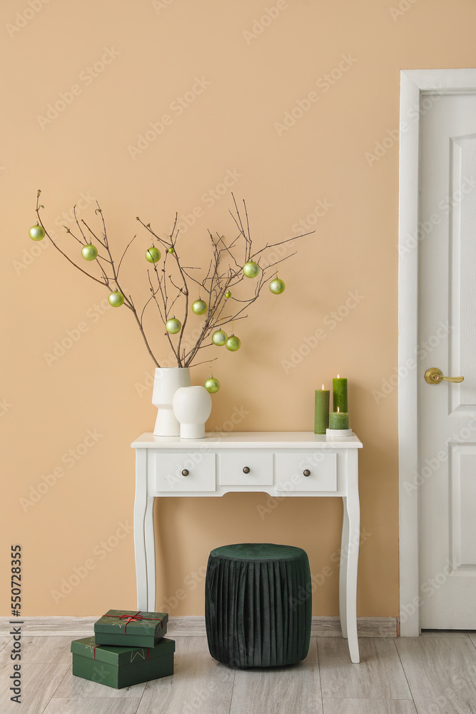 Vases with tree branches, Christmas balls and candles on table in living room