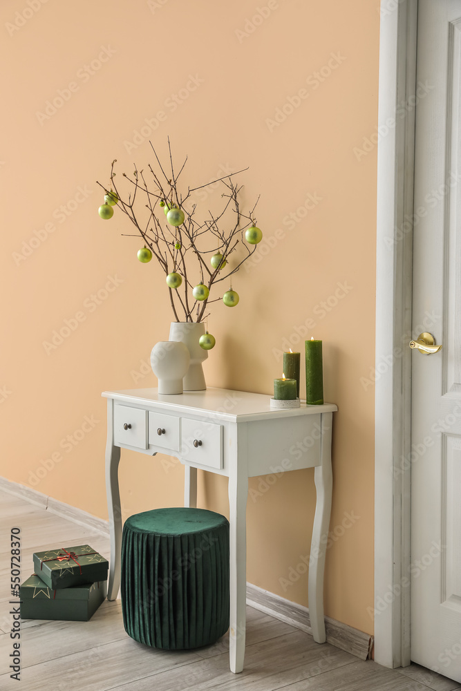 Vases with tree branches, Christmas balls and candles on table in living room