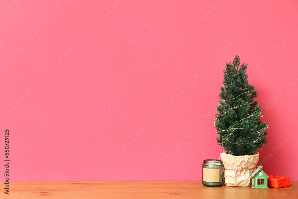 Small Christmas tree, candle and gifts on table near red wall