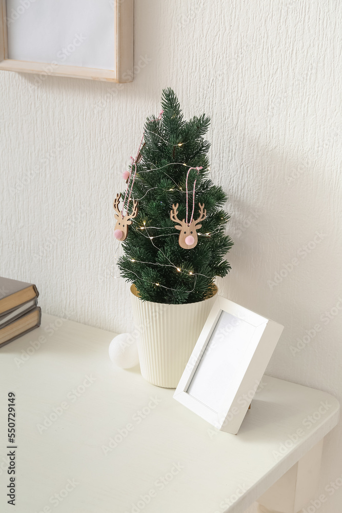 Small Christmas tree with frame on table near light wall