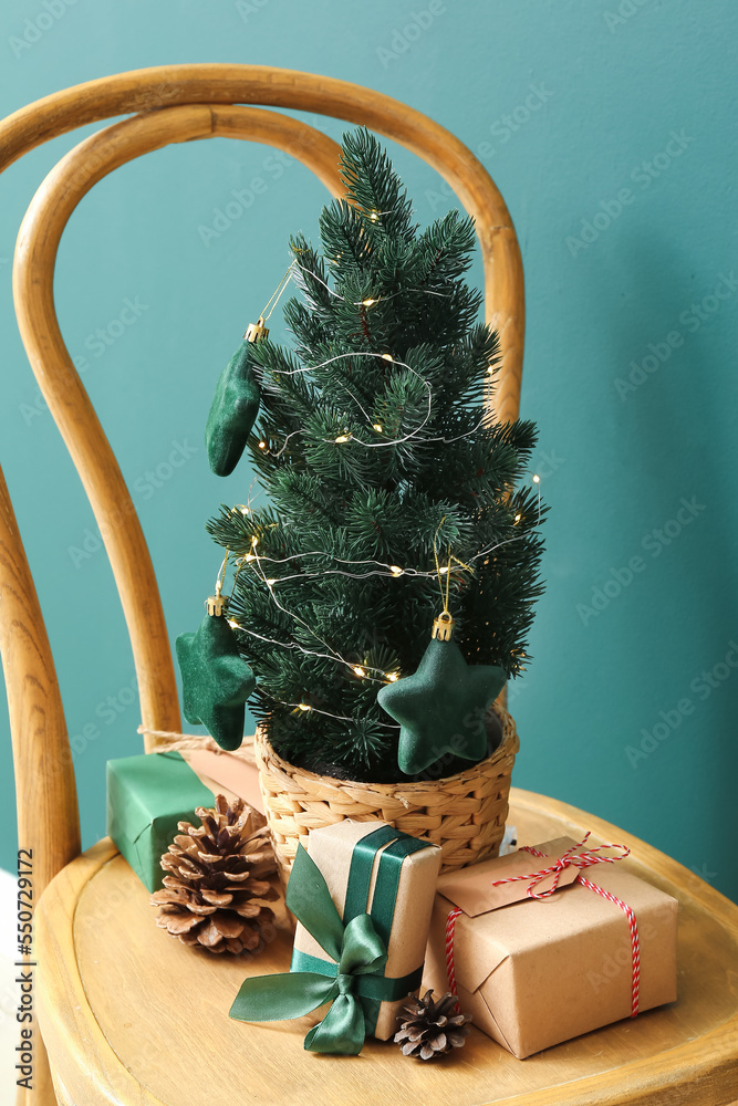 Small Christmas tree with pine cones and gifts on chair near green wall, closeup