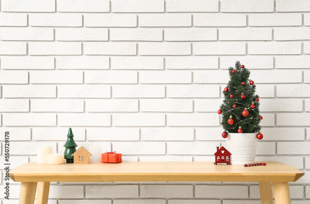 Small Christmas tree with toys on table near white brick wall